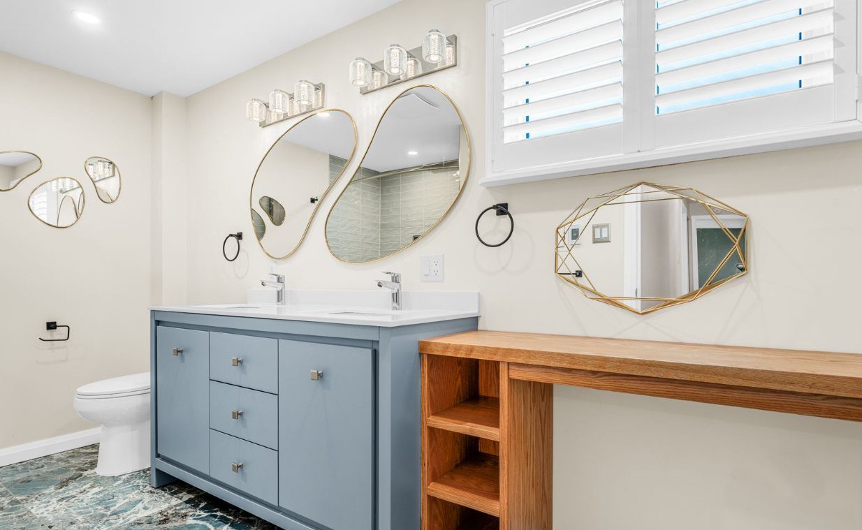 Bathroom remodel with a blue double vanity, round mirrors and a wood makeup counter