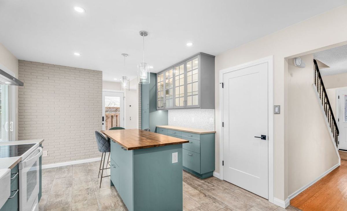 Renovated kitchen with a wood-top island, glass-front upper cabinets and a painted brick wall
